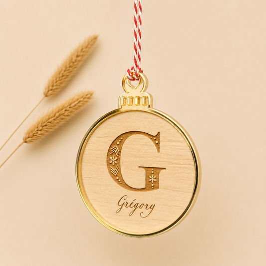 Décoration de Noël personnalisée en bois avec prénom et initiale gravés. Son contour miroir apporte une touche élégante à cette boule de Noël artisanale, idéale pour décorer le sapin.
